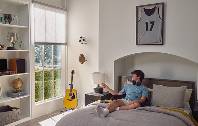 Person seated in a bedroom using the Pico Remote to raise smart shades on a sunny window.